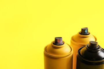 Spray paint cans on yellow background, closeup