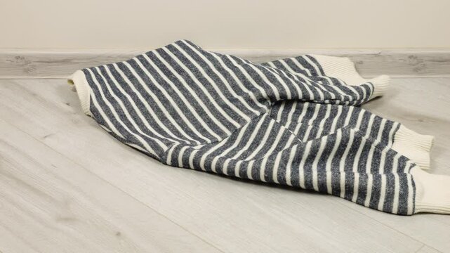 Knitted sweaters, scarves, woolen hats in gray-blue tones are thrown on the floor in the room. The theme of washing, sorting clothes and cleaning the house.