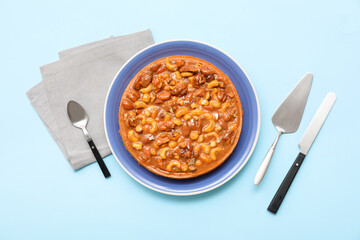 Plate of sweet tart with different nuts and caramel on blue background