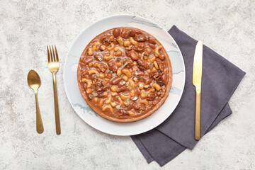 Plate of sweet tart with different nuts and caramel on white background