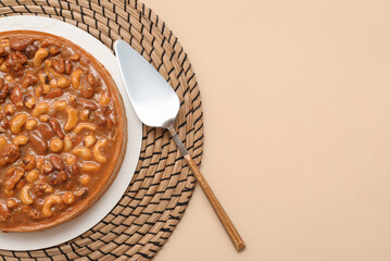 Plate of sweet tart with different nuts and caramel on beige background
