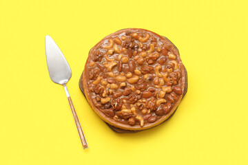 Wooden board of sweet tart with different nuts and caramel on yellow background