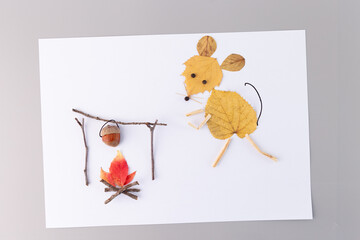 Mouse made of yellow autumn leaves standing near a campfire with a pot hanging from twigs, acorn...