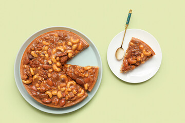 Plates of cut sweet tart with different nuts and caramel on green background