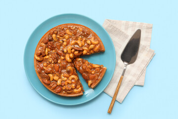 Plate of cut sweet tart with different nuts and caramel on blue background