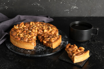 Boards of cut sweet tart with different nuts and caramel on black background