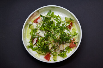 Salad dish with lettuce, tomatoes, and cucumbers on a black plate