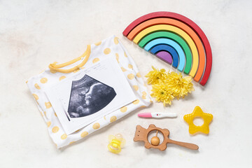Composition with baby clothes, sonogram image, pregnancy test and toys on grunge beige background