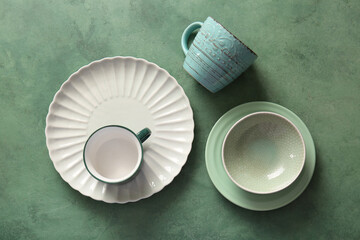 Clean cups, bowl, saucer and plate on green grunge background. Top view