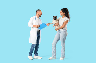 Male veterinarian with owner holding pug dog's paw on blue background
