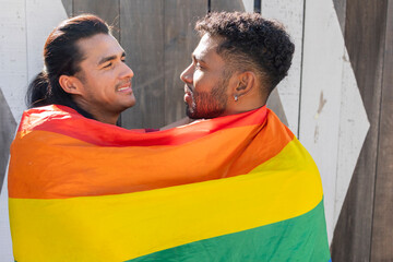 Gay couple wrapped in pride flag sharing a loving moment