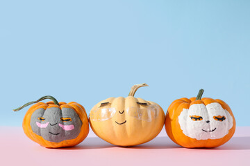Pumpkins with drawn faces, clay masks, under-eye patches and eyelashes on pink table near blue wall
