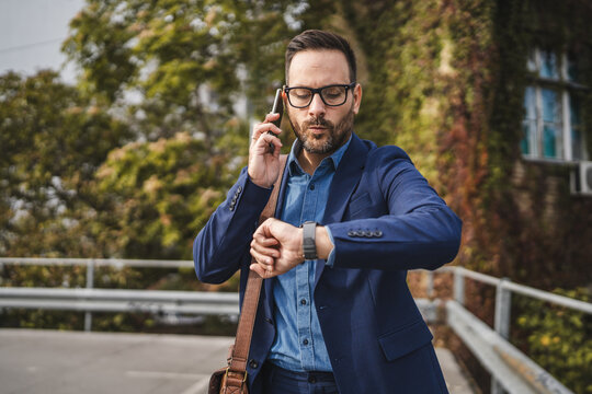 Wistful businessman talk on mobile phone and check time on wrist watch