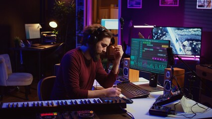 Musician artist taking notes composing new song in his home studio, writing down lyrics and musical notes before recording his melody. Songwriter producing music with daw software tools. Camera B.