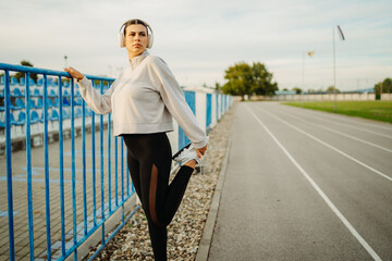 Fototapeta premium Young caucasian woman stretching and resting after run on stadium track