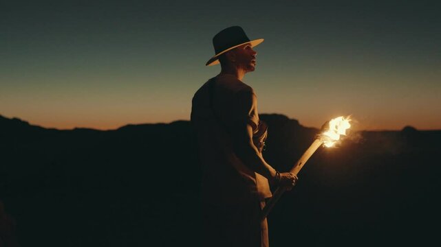 In the soft light of the evening, a man ascends towards the desert arch, casting light upon the rock with his torch