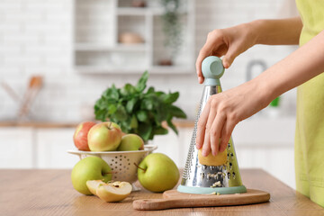 Young woman grating fresh apple in kitchen
