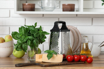 Grater, ingredients and wooden cutting board on table near white brick wall in kitchen