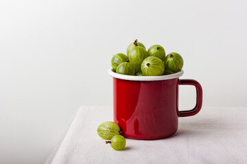 Fresh green gooseberry berries in a red enamel mug