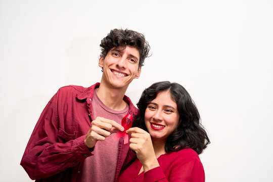 Young Latin couple, holding red ribbon for World AIDS Day - Powered by Adobe