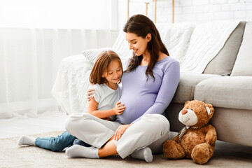 Family concept. Adorable little girl cuddling with her expecting mother at home, sitting on floor...