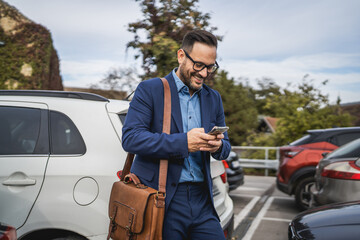 Adult businessman stand in the parking lot and use mobile phone