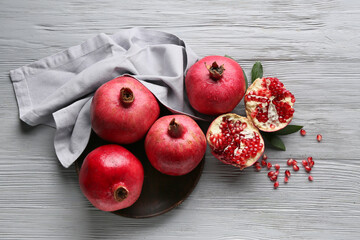 Plate with fresh ripe pomegranates and seeds on grey wooden background