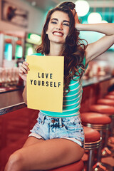 Portrait, smile and woman with paper to love yourself, affirmation or empowerment at retro diner....