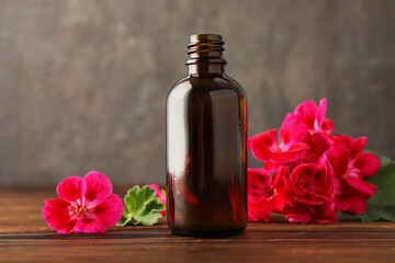 Geranium essential oil in bottle and beautiful flowers on wooden table