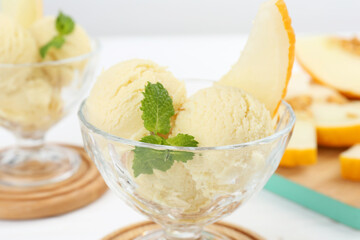Scoops of melon sorbet with mint and fresh fruit in glass dessert bowls on white table, closeup