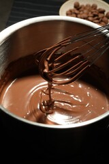 Chocolate dough dripping from whisk into bowl on table, closeup