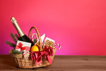 Wicker gift basket with wine on wooden table against pink background, space for text