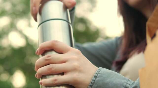 Woman is opening thermos and putting it next to metal cup on the bench filmed in closeup slow motion. Macro view of Caucasian lady preparing to have hot drink from metal bottle outdoors. Break time