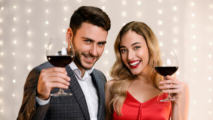 Cheers. Attractive Man And Woman Holding Glasses With Red Wine, Toasting And Smiling At Camera, Celebrating Holidays
