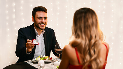 Romantic Proposal. Loving Man Asking His Girlfriend To Marry Him On Date In Restaurant, Selective Focus, Free Space