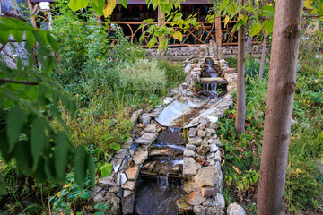 A stone-lined stream with a waterfall and a lush green garden