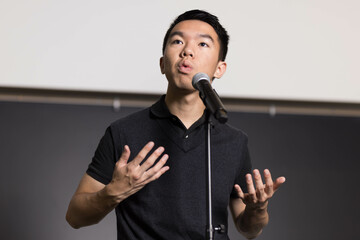 A young man confidently speaks to an audience in front of a microphone