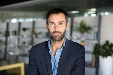 Confident handsome middle aged Caucasian business leader man in casual jacket looking at camera, standing in co-working, posing for head shot. Serious businessman, entrepreneur, CEO portrait