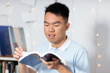 A teen boy reading a book in his room at home