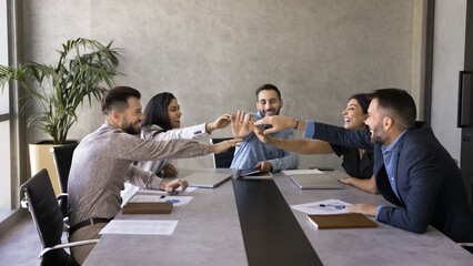 Happy multiethnic team giving group high five, clapping hands over meeting table, laughing, enjoying celebrating successful teamwork, achievement, startup project success. Banner shot