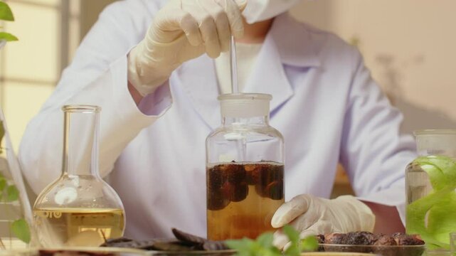 The video, set in a warm, modern lab, features a researcher stirring a soapberry solution in a cork bottle, surrounded by other herbs and solutions on the table.