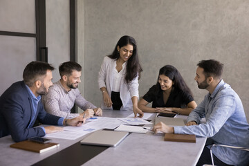 Multiethnic business team of positive young colleagues analyzing marketing data, talking at meeting...