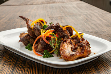 Grilled or roasted meat, arranged artfully on a white platter. The meat is cooked to a golden-brown, crispy texture, giving it a mouthwatering, caramelized appearance. 