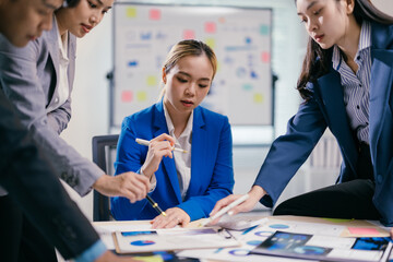Diverse team of asian businesspeople collaborate in a busy office, analyzing charts and strategizing for success