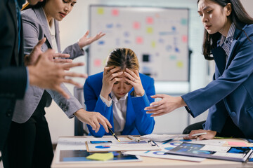 Businesswoman is feeling overwhelmed and stressed as her coworkers stand around the table, pointing...