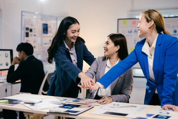 Three businesswomen celebrating successful teamwork in a diverse office meeting, showing unity and trust. Capturing collaboration and support in a corporate setting