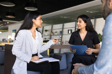 Serious busy young Indian project manager speaking to Arab colleague at team meeting, sharing creative ideas for teamwork, cooperation. Diverse group brainstorming on project strategy.