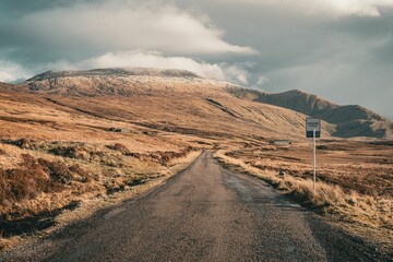 Scenic road leading through a mountainous landscape under a cloudy sky in Scotland