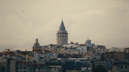 Obraz premium View of Galata Tower surrounded by buildings under a cloudy sky in Istanbul, Turkey