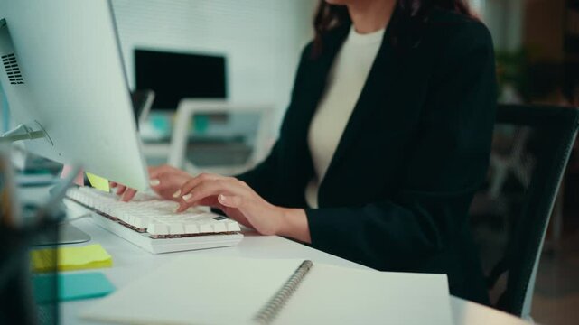 Businesswoman sitting at a desk in an office, typing on a keyboard while working on a computer. Focused and engaged, she manages tasks and correspondence efficiently
